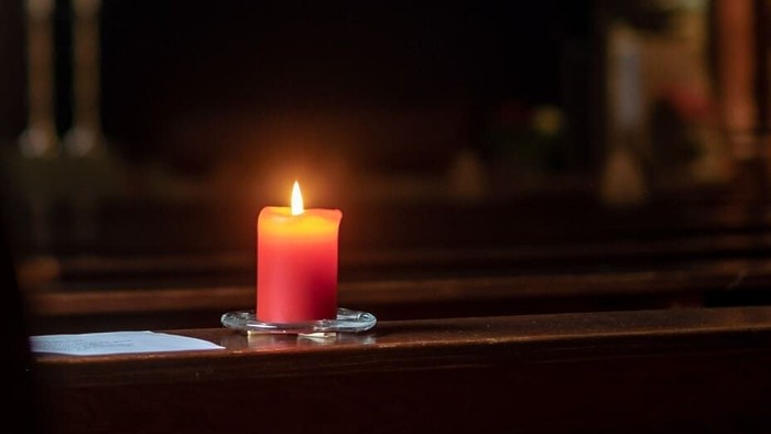 Eine brennende rote Kerze steht auf einem Tisch in einem dunklen Raum.