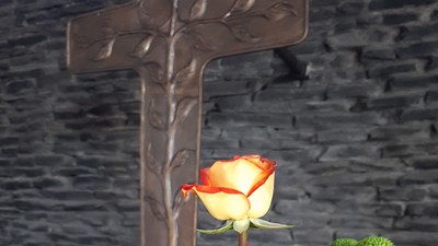 Ein Holzkreuz vor einem Blumenstrauß mit Sonnenblumen und Rosen
