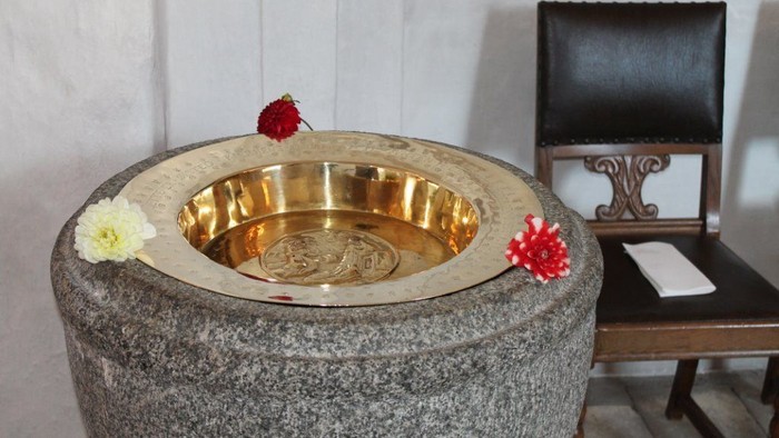 En stor steenbassin med guldfarvet indel og blomster på kantene, ved siden af en stol med noter.