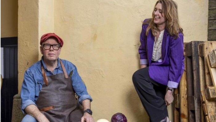 Foto af Claus Holm siddende med forklæde og Signe Rye stående, grønsager imellem den