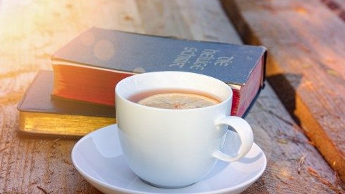 Eine Tasse Kaffee steht neben Büchern auf einem Holztisch.