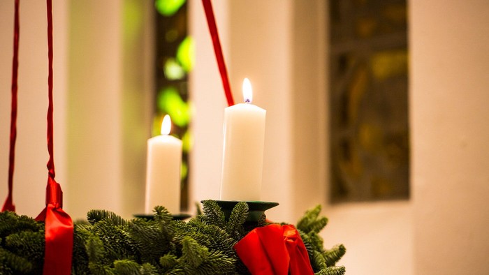 En julekrans med to lysende lysekøn og røde bælter.