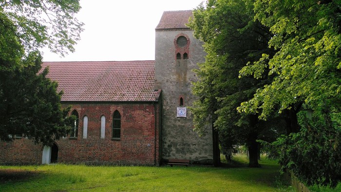Alte Backsteinkirche mit Turm, umgeben von grünen Bäumen und Wiese