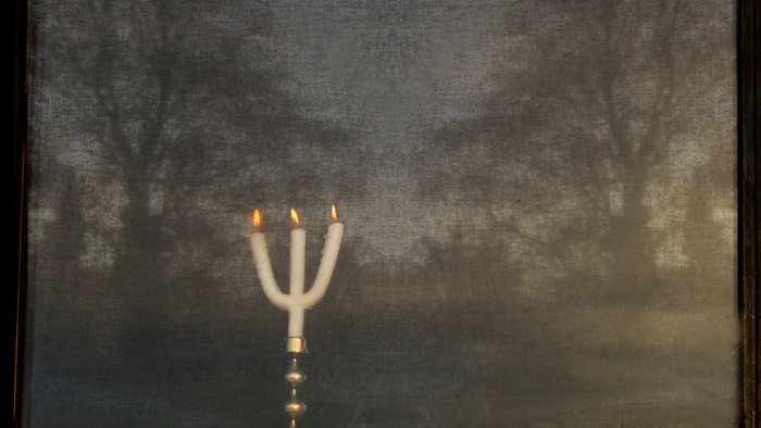 En lysestage med tre lys på en mørk vej med træer.