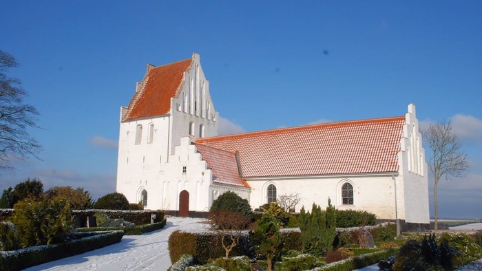 En hvid kirke med røde tag i snødekkede omgivelser