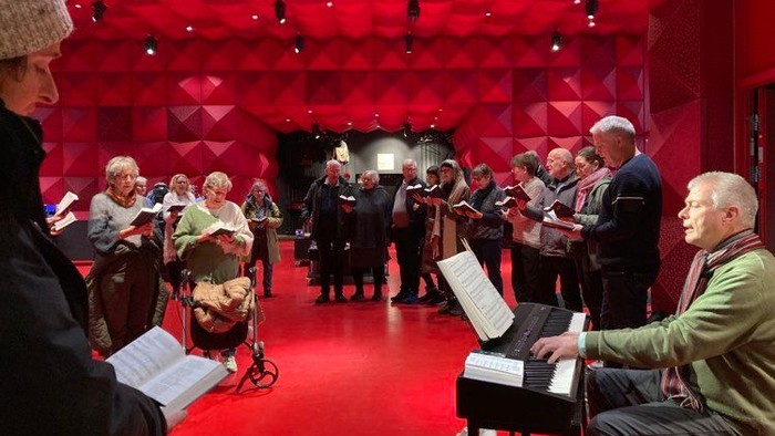 En gruppe mennesker synger i et rødt rum med musikalske noter.
