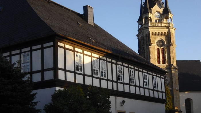 Traditionelles Fachwerkhaus neben einer hohen Kirche mit Uhrturm.