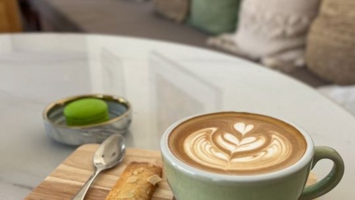 Ein Löffel, ein Keks und eine Tasse Kaffee mit vielen Herzen im Schaum