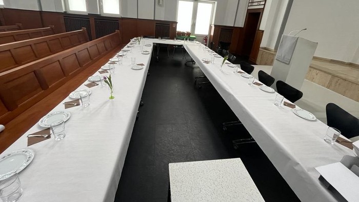 Zwei Tischreihen stehen im vor dem Altarraum mit weißen Tischdecken, Tellern, Gläser, Servietten und Besteck.