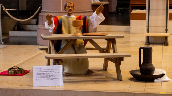 Drei Figuren sitzen an einem Picknicktisch, eine davon hält ein Schild.