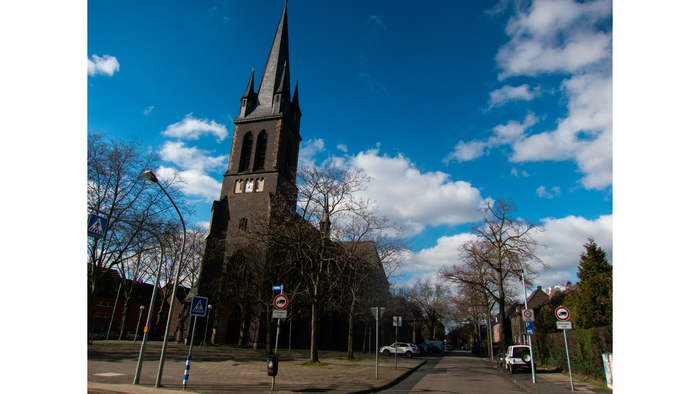 Kirchturm vor blauem Himmel und Bäumen
