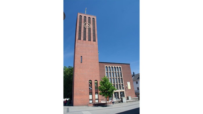 Grosse Kirche mit hohem Turm und Uhr, umgeben von Bäumen und Gebäuden