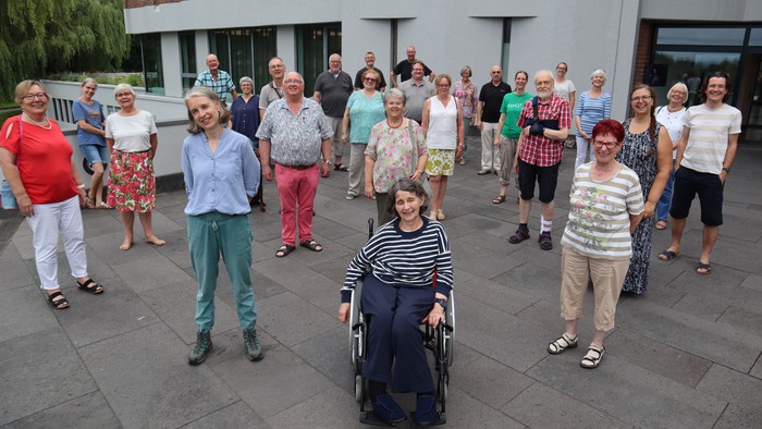 Eine Gruppe von Menschen steht vor einem Gebäude, eine Person sitzt im Rollstuhl