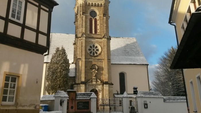 Gotischer Kirchturm mit Uhr und Kreuzigungsgruppe vor historischem Hintergrund