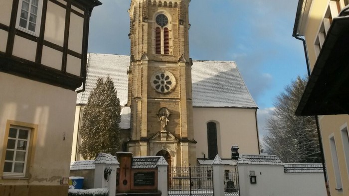 Gotischer Kirchturm mit Uhr und Kreuzigungsgruppe vor historischem Hintergrund