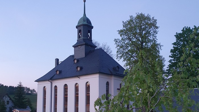 Kirche mit Friedhof und Bäumen im Hintergrund