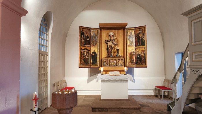 Ein kleiner Altarraum mit einer Madonnenstatue und mehreren Gemälden in einem weißen Gewölbe.