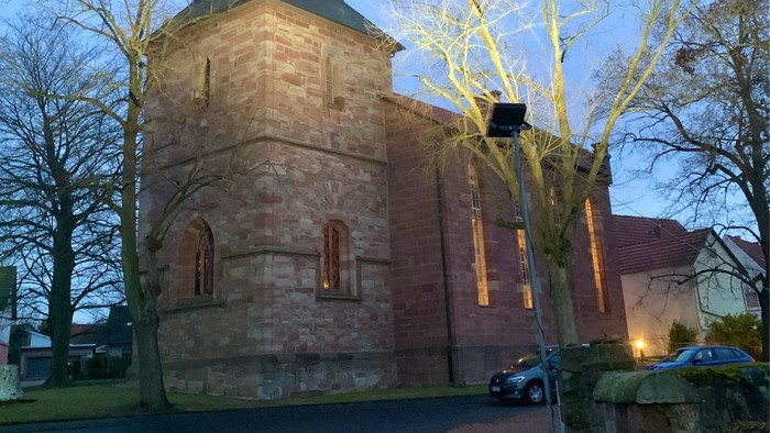Kirchturm mit Uhr und spitzen Dach bei Dämmerung