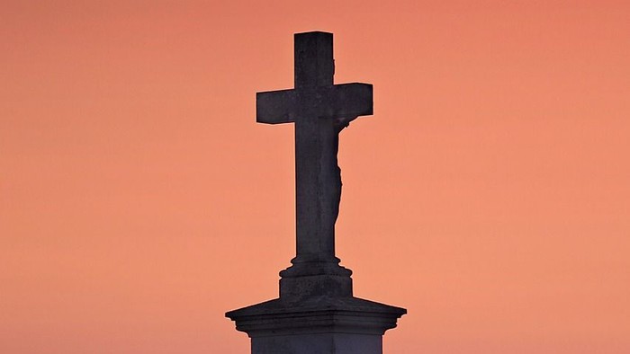 Ein Kreuz steht auf einem Hügel bei Sonnenuntergang