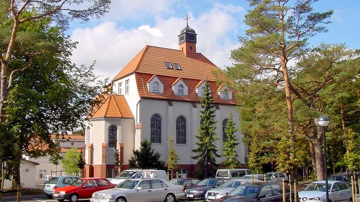 Parkplatz vor weißem Gebäude mit rotem Dach und Turm.