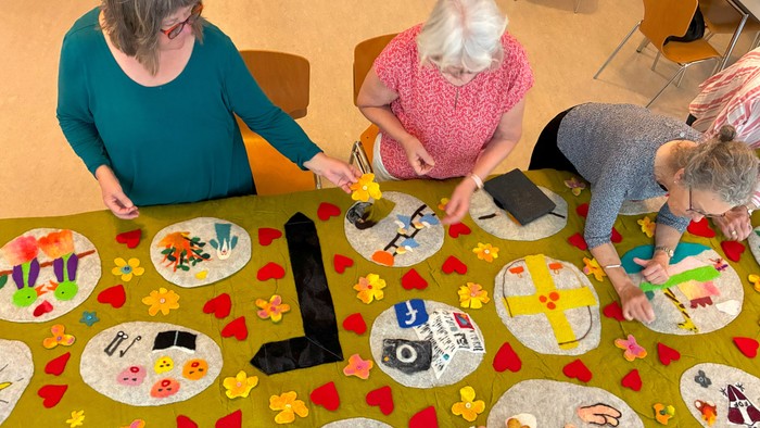 En gruppe af voksne og børn sidder om en bord og laver håndarbejde med papir og kleber.