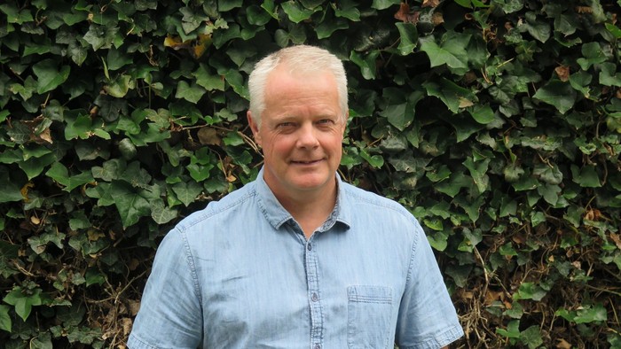 En blond mand i blå skjorte står foran en grøn klædende.