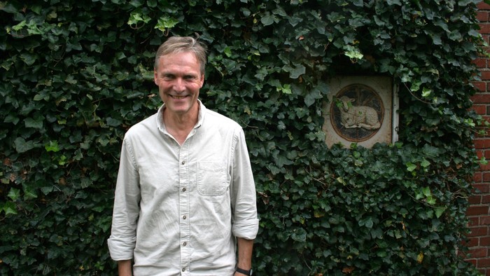 Mand, der står foran en mur dækket af vedbend.