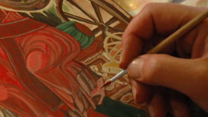 En kunstner maler omhyggeligt indviklede blomstermønstre med en fin pensel på et lærred.