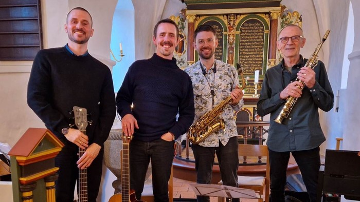 En kvartet af musikere, der holder forskellige instrumenter i en kirkesal og poser sammen.