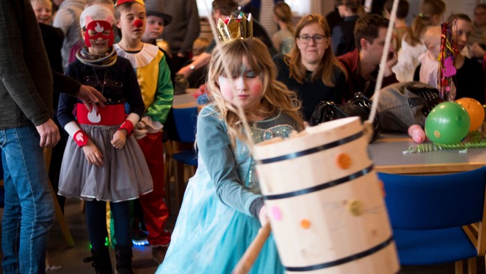 En pige i blå kagepudderkostume slår på en tønde med en kølle.