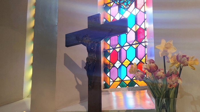 Ein Altar mit Kreuz, Kerzen und Blumen vor einem buntem Kirchenfenster