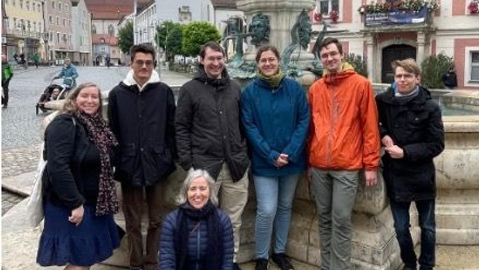 Eine Gruppe von sieben Personen posiert vor einem Brunnen in einer historischen Stadt.