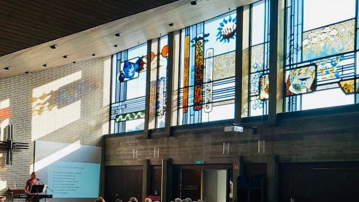 Große Menschenmenge vor modernem Gebäude mit bunten Glasfenstern