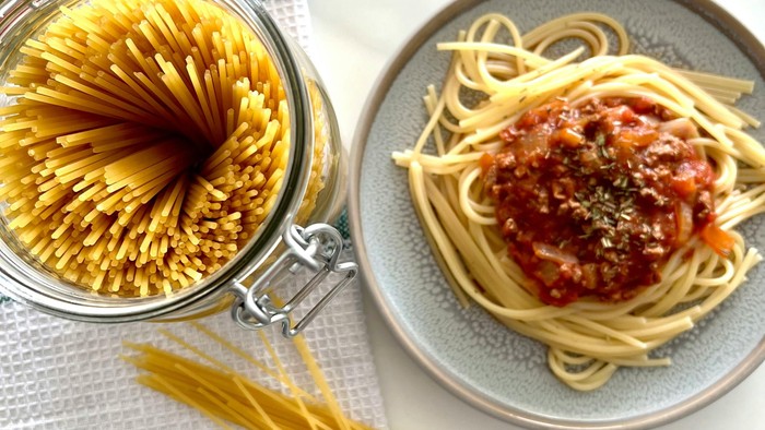 Frisk spaghetti med tomatsauce serveret på en tallerken ved siden af ubrygget pasta i en krukke.