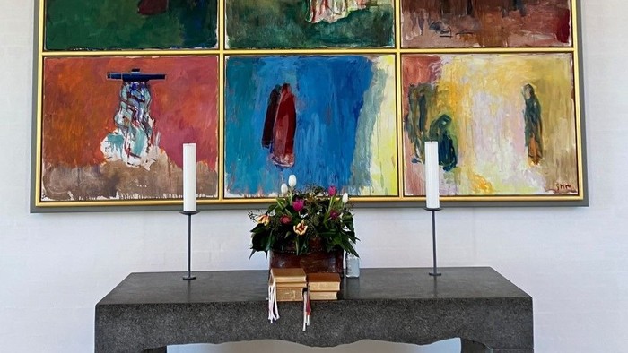 En række farvede malerier på veggen over en bord med blomster og lysstake