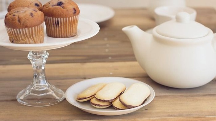 A wooden table with muffins, cookies, and a teapot.