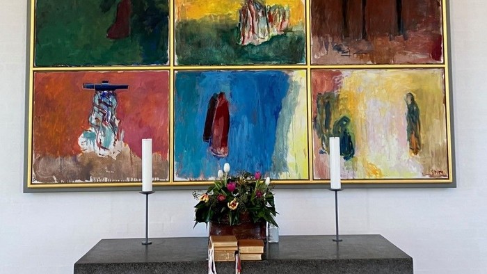 En række farvede malerier på veggen over en bord med blomster og lysstake