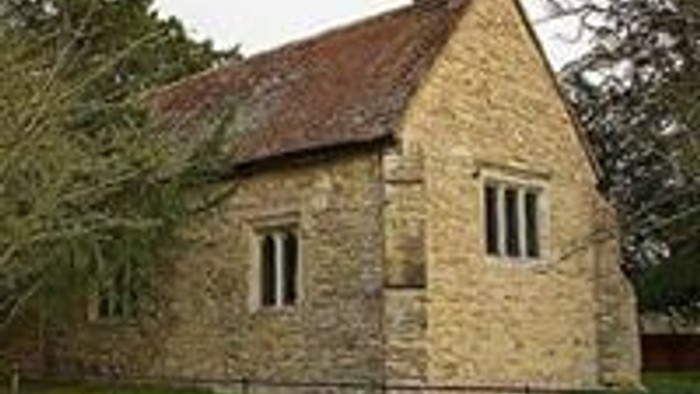 Small stone building with a pitched roof, surrounded by a metal fence and trees.