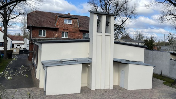 Modernes weißes Gebäude mit einzigartiger Architektur, umgeben von Bäumen und anderen Häusern.