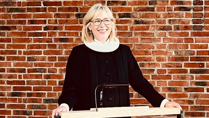 Kvinde ved pulpet forud for mur af røde teglsten