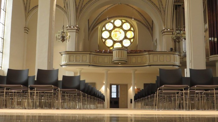 Innenraum einer Kirche mit Säulen, Stühlen und einem großen Fenster.