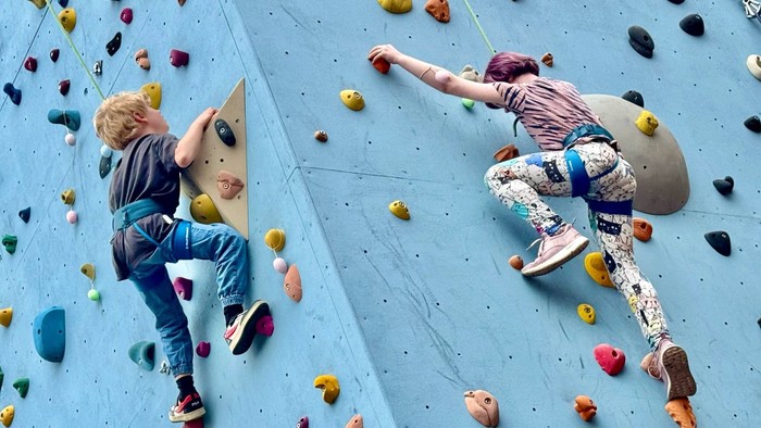 To børn klatrer på blå klatrevæg.