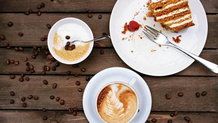 Ein Stück Kuchen, eine Tasse Kaffee und eine kleine Schale mit Zucker auf einem Holztisch