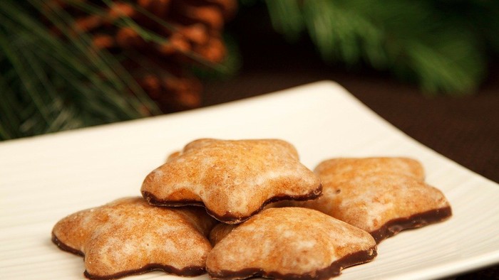 Weihnachtliche Plätzchen auf weißem Teller mit Tannenzapfen und Beeren im Hintergrund