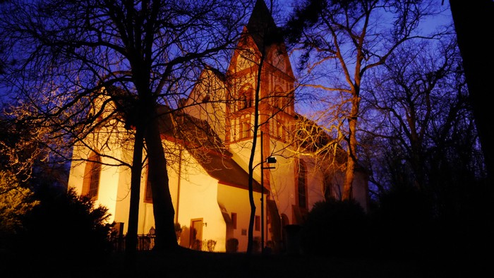 Ein beleuchtetes Kirchengebäude bei Nacht, umgeben von Bäumen