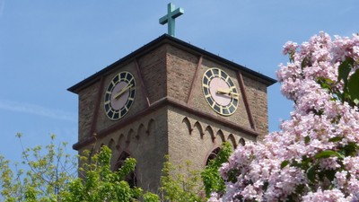 Uhrturm mit Zifferblatt und Kreuz, umgeben von blühenden Bäumen