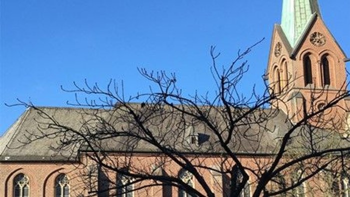Ein Kirchengebäude mit hohem Turm und spitzen Dach unter blauem Himmel.