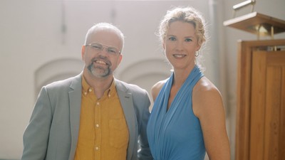 Par, der poser sammen, mand i gul skjorte og grå blazer, kvinde i blå kjole.