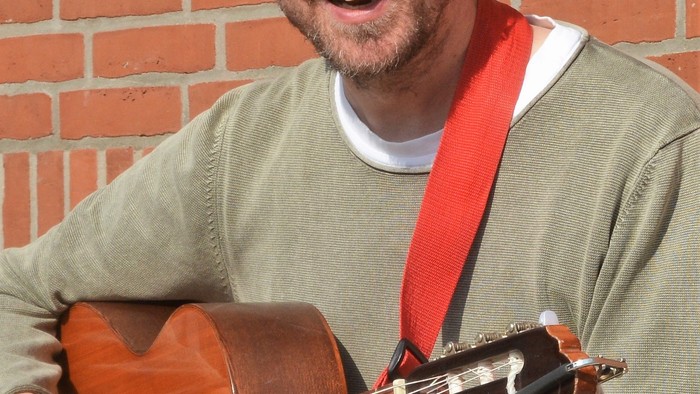 Mand der spiller guitar og smiler