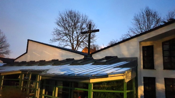 Ein Haus mit grünem Gewächshaus und Kreuz auf dem Dach vor blauem Himmel